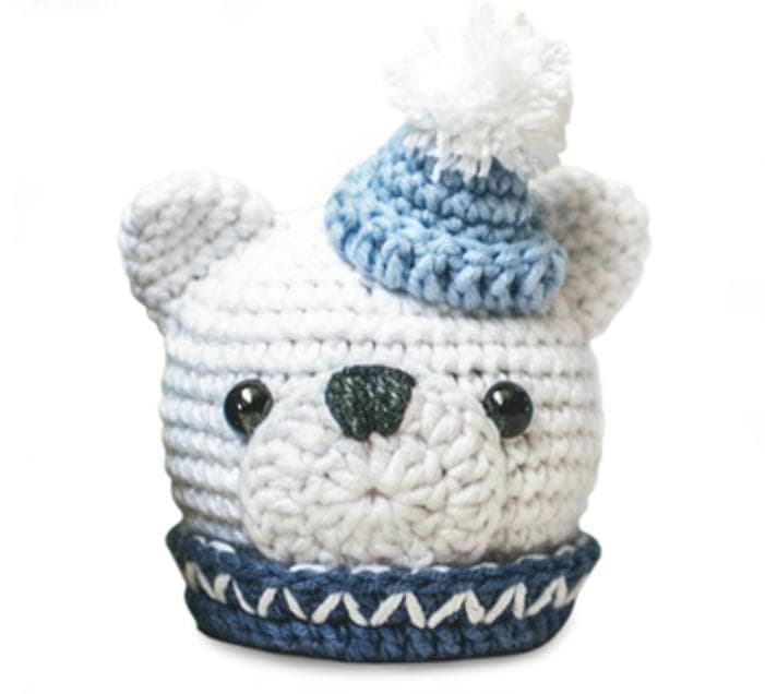 Close-up of a crocheted white bear's face, featuring black safety eyes, an embroidered nose, and a cute light blue knitted hat