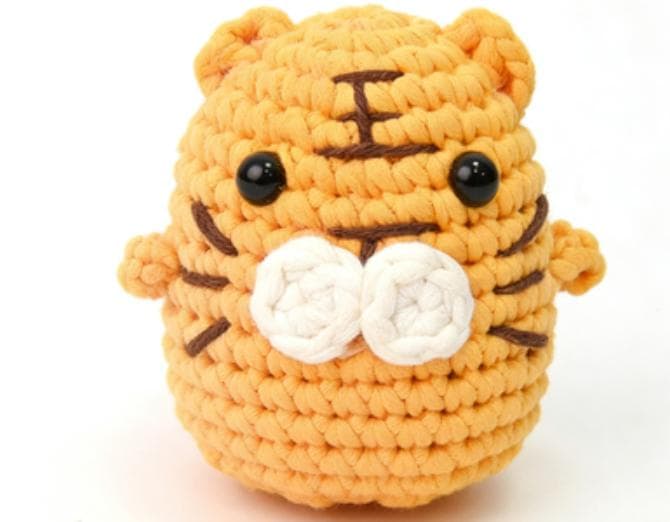 Handmade chubby orange tiger crochet stuffed animal featuring brown embroidered stripes, a white puffy muzzle, and black safety eyes.