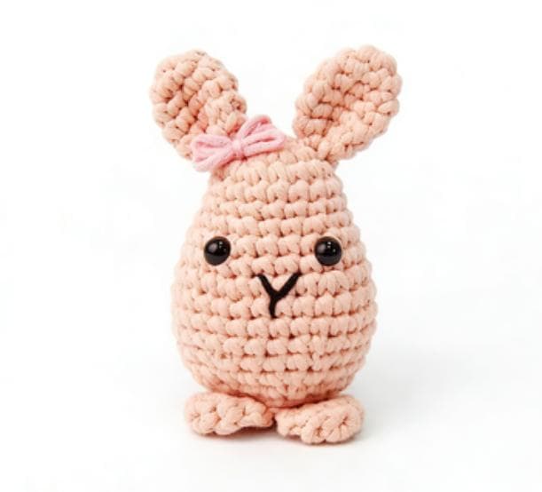 Kawaii egg-shaped rabbit amigurumi plushie made with pastel pink chunky yarn, perfect as a cute desk pet or handmade gift.