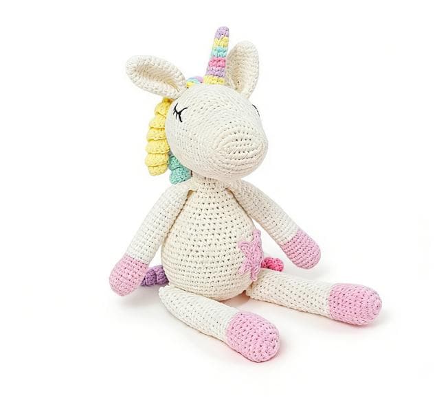 Handmade white unicorn crochet stuffed animal. A cute ragdoll-style amigurumi plushie featuring a pastel rainbow mane and horn, pink hooves, sleeping eyes, and a pink star on its belly, perfect as magical nursery decor or a finished handmade gift.